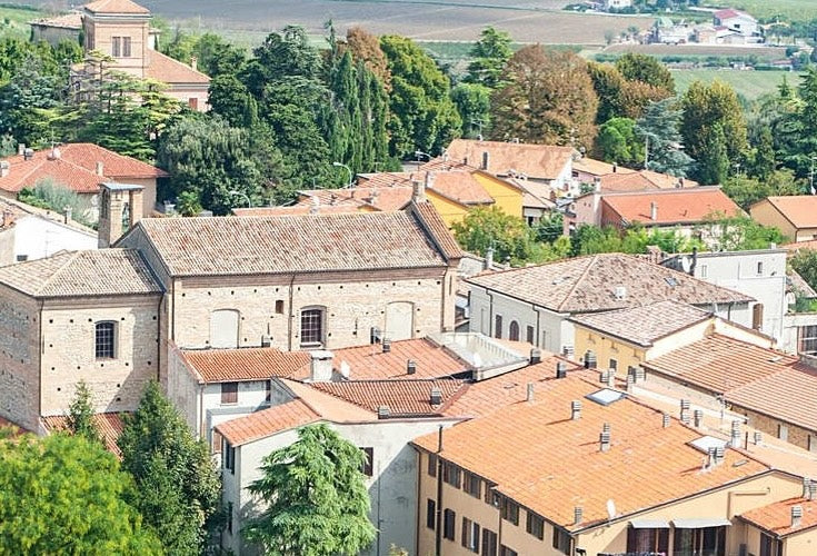 Aerial view of rustic town with terracotta rooftops, surrounded by lush greenery and countryside.