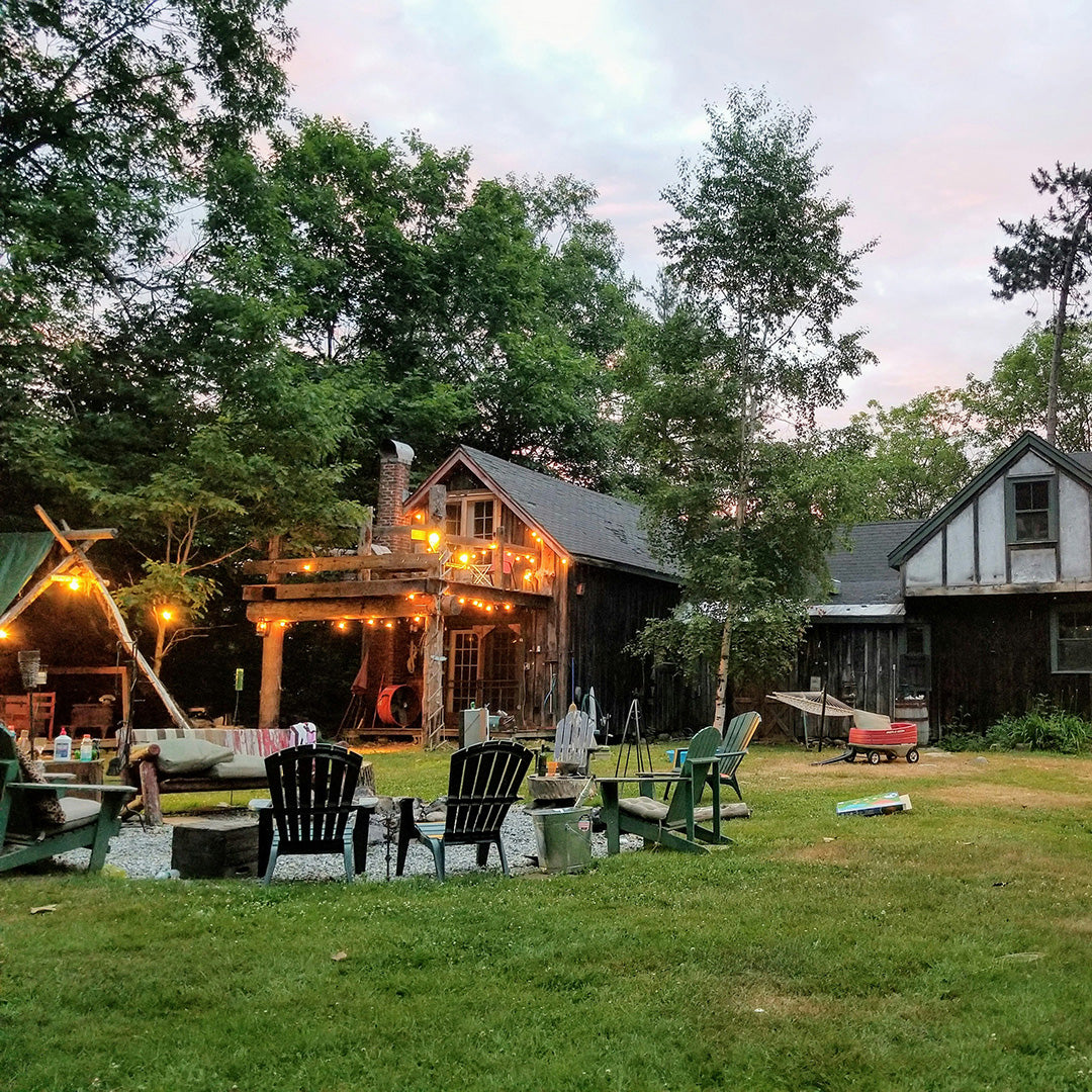 Rustic cabin with string lights, surrounded by trees and lawn chairs, creating a cozy outdoor setting.
